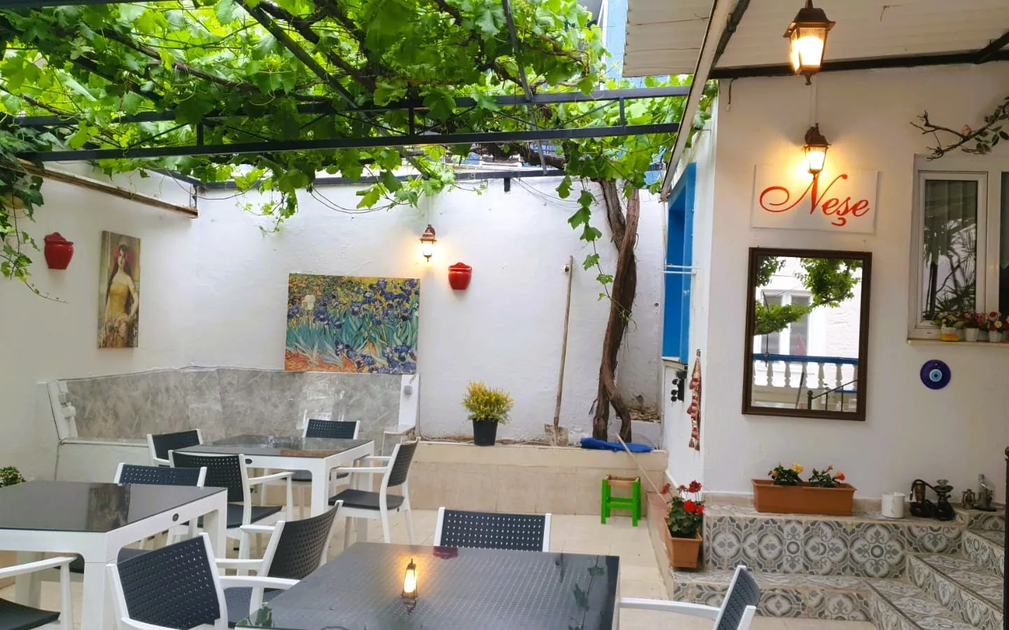 Neşe Hotel Çeşme — Sitzbereich im Garten unter der Weinpergola mit Wandbildern
